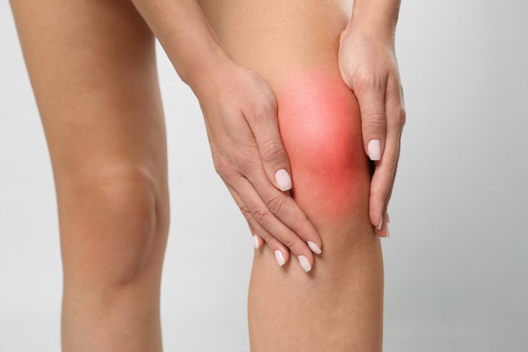 Woman having knee problems on grey background, closeup