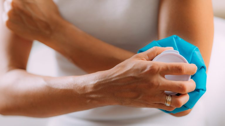 Elbow pain treatment. Woman holding an ice bag compress on a painful elbow